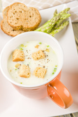 Asparagus soup with croutons on a mug with crusty bread slices