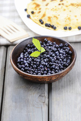Wooden bowl of blueberries, pancakes in the background