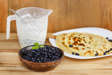 Wooden bowl of blueberries, pancakes and mousse in jug. Ingredie