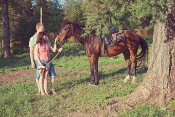 Young couple with purebred brown horse outdoors, horizontal shot