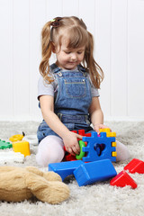 Happy little girl play colorful toys on soft carpet at home.