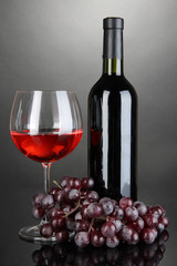 Obraz premium Red wine glass and bottle of wine on grey background