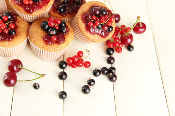 Tasty muffins with berries on white wooden table