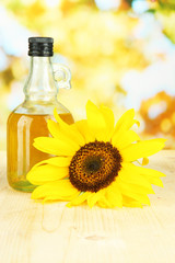 Oil in jar and sunflower on wooden table close-up