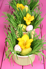 Easter eggs in bowls with grass on pink wooden table close up