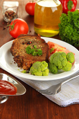 Piece of fried meat on plate on wooden table close-up