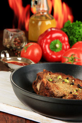 Piece of fried meat on pan on wooden table on fire background