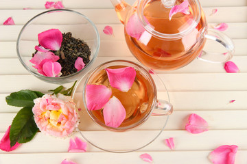 Kettle and cup of tea from tea rose on wooden background