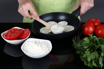 Hands cooking marrows in pan on gray background