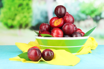 Ripe plums in bowl on wooden table on natural background
