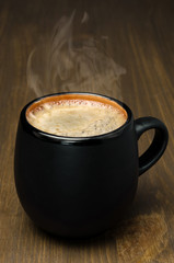 black mug of coffee with foam on a wooden table