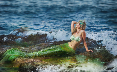Beautiful fashionable mermaid sitting on a rock by the sea