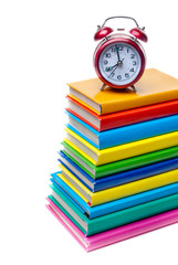red clock on top of a stack of colored books isolated on white