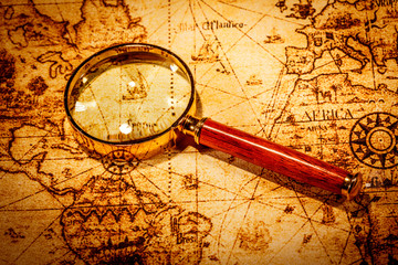 Vintage magnifying glass lies on an ancient world map