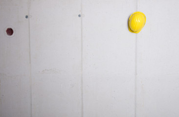 Yellow hard hat hanging on a grey concrete wall