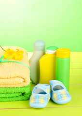 Baby cosmetics, towels and boots on green wooden table