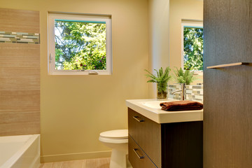 Beige modern new bathroom with brown wood cabinets and tub.
