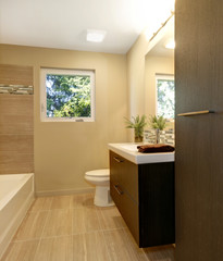Fototapeta na wymiar Beige modern new bathroom with brown wood cabinets and tub.