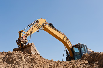 Ein Bagger auf einem grossen Erdhaufen unter blauem Himmel