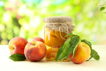 Jar of canned peaches and fresh peaches on wooden table,