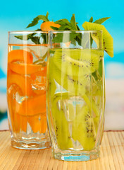 Glasses of fruit drinks with ice cubes on blue background