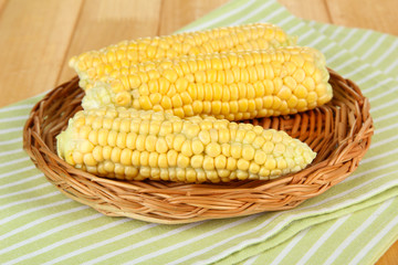 Fresh corn on wicker mat, on wooden background