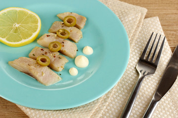 Dish of herring and lemon on plate on wooden table close-up