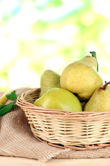 Pears in basket on burlap on wooden table on nature background