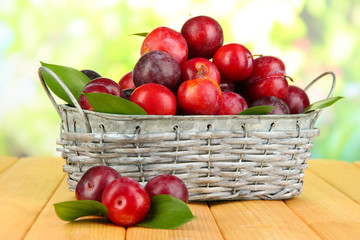 Ripe plums in basket on wooden table on natural background