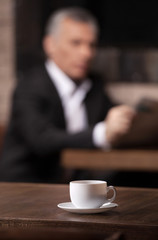 Break time. Mature businessman reading a newspaper with a cup of