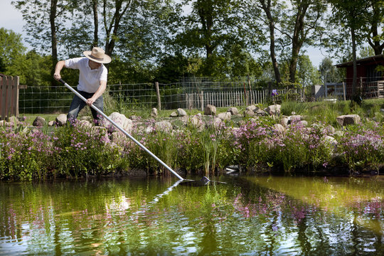 G&auml;rtner mit Strohhut reinigt seinen Teich