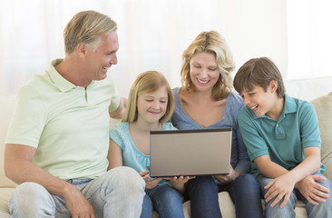 Fototapeta na wymiar Parents And Children Using Laptop Together On Sofa