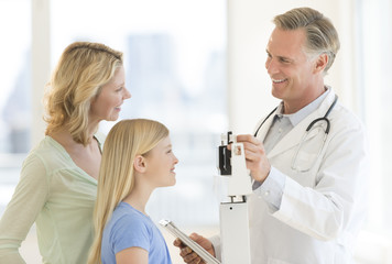 Doctor Examining Girl's Weight While Looking At Woman In Clinic