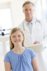 Fototapeta premium Girl Smiling With Doctor Standing In Background At Clinic