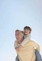 Father Giving Piggyback Ride To Son Against Clear Blue Sky