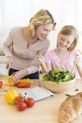 Obraz na płótnie Canvas Girl Assisting Mother In Preparing Salad At Counter