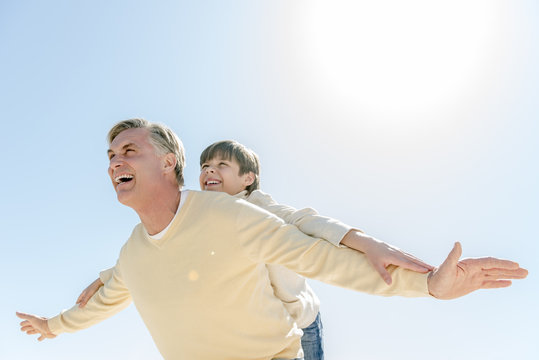 Man Giving Piggyback Ride To Son Against Clear Blue Sky