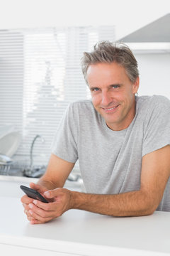 Smiling man texting in kitchen