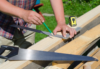 Male hands measuring and marking wooden plank outdoors