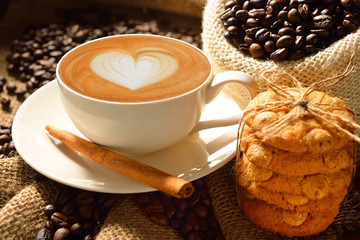 A cup of cafe latte with coffee beans and cookies