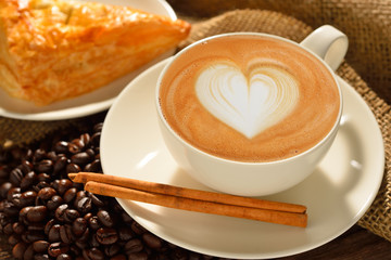 A cup of cafe latte with coffee beans and puff pastry