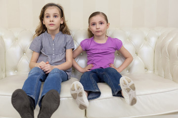 Two girls sitting on sofa in shoes and watching TV