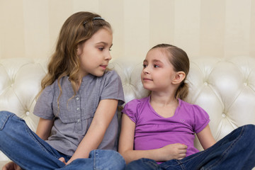 Two girls sitting on sofa and looking at each other