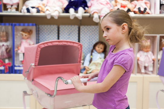 Girl in toy store with many dolls purchased buggy
