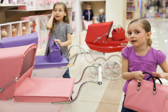 Two girls in toy store with rows of dolls purchased buggy