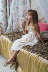 A little girl sits on a large bed and yawns