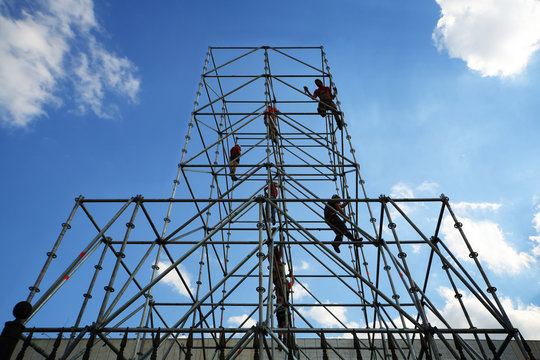 Workers Working On Tall Scaffolding Against A Blue Sky