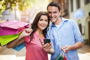 Happy couple using smart phone during the shopping .