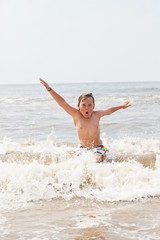 Fototapeta premium Kid boy having fun at the beach in the waves of the ocean.