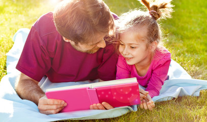 Father reading a book to his daughter in the garden